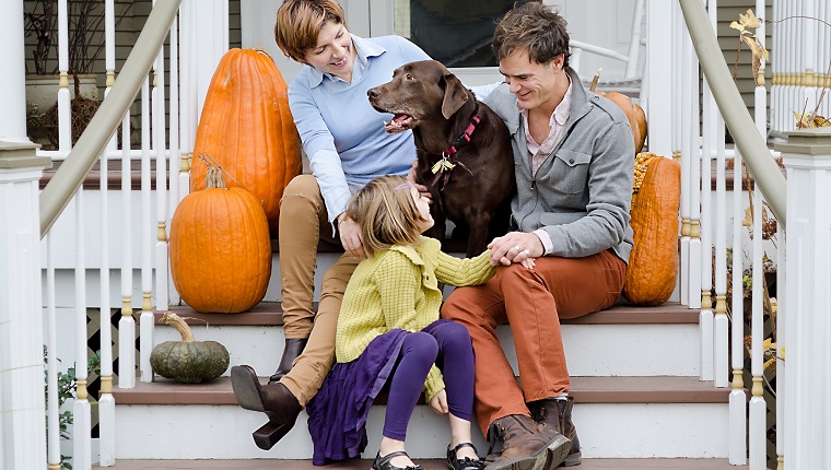Glückliche Familie, die vor Haus mit Hund und Kürbisen sitzt