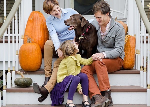 Happy Family Sitting In Front of House with Dog and Pumpkins
