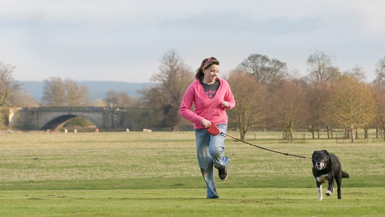 Teenager mit ihrem Hund läuft durch einen Country Park