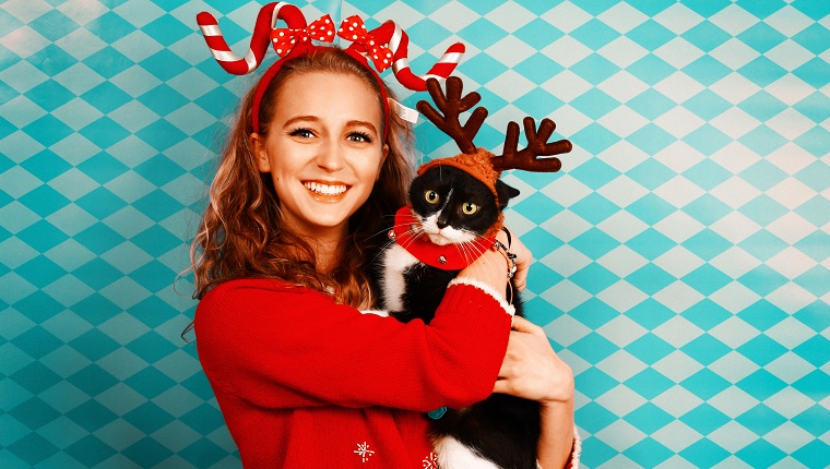 Ein Mädchen, das für eine Weihnachtskarte trägt ein Zuckerstangekopfband aufwirft, das ein tragendes Elchgeweih der schwarzen Katze hält.