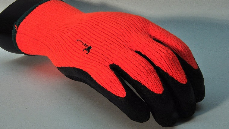 Ein orangefarbener Handschuh mit schwarzem Griffmaterial an den Fingern wird auf grauem Hintergrund angezeigt.
