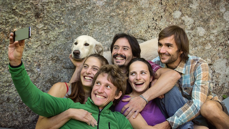 Eine Gruppe von Wanderfreunden macht ein Selfie mit einem Golden Retriever vor einem Felsen.
