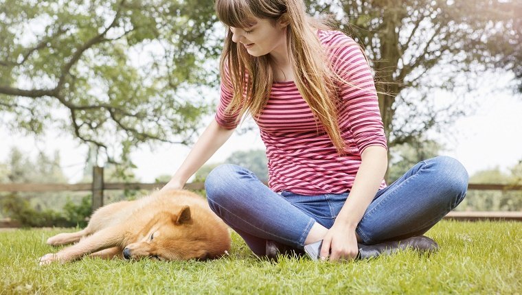 Yung Frau streichelt Hund, der im Gras döst.