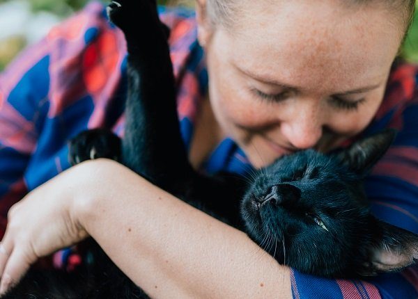Portrait of blondhaired woman hugging her black cat outdoor.