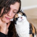 Young woman bonding with calico cat bumping rubbing bunting heads, friends friendship companion pet happy affection bonding face expression, cute adorable kitty