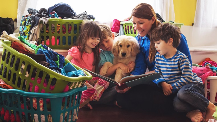 Lächelnde Mutter liest vor drei Kindern und Golden Retriever Hündchen, umgeben von Wäschekörben