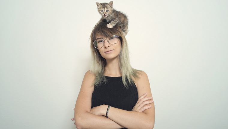 Porträt einer jungen Frau mit ihrer Katze über dem Kopf.
