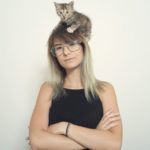 Portrait of a young woman with her cat over her head.