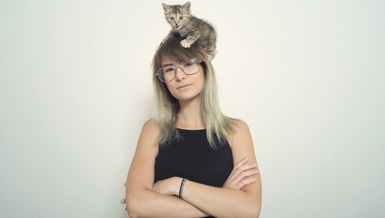 Portrait of a young woman with her cat over her head.