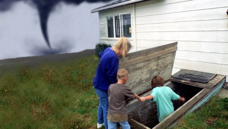 Eine Familie betritt einen Sturmkeller, während ein Tornado im Hintergrund aufsetzt.