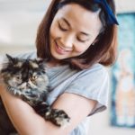 Pretty young lady holding a fluffy cat in her arms joyfully