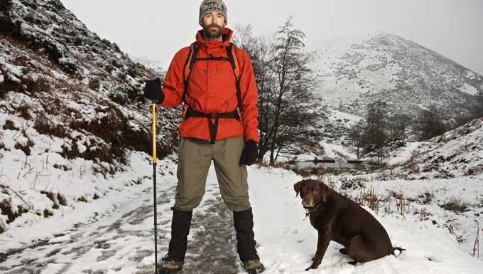 Mensch und Hund wandern in schneebedeckten Bergen