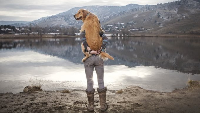 Mann hält Hund in der Nähe von See und Bergen