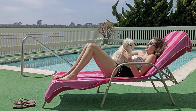 Frau, die auf Loungesessel durch Schwimmbad niederlegt und Hund auf ihrem Bauch hält