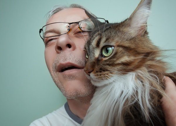 A dishevelled and sickly looking man hugging his beautiful Maine Coon Cat.