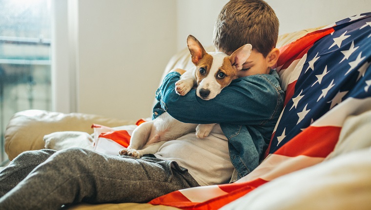 Junge und ein Hund sitzen auf dem Sofa zu Hause mit amerikanischer Flagge