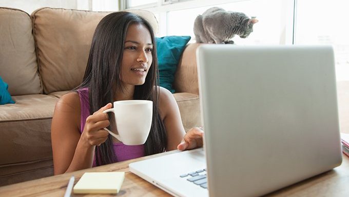 Frau auf Laptop mit Katze im Hintergrund