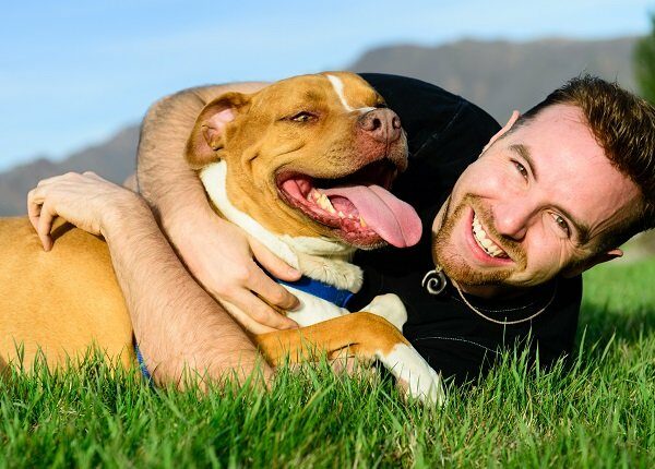 Happy male with his dog on the grass. Mountain range and clear sky in background.
