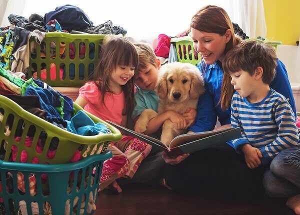 Smiling mother reading to three children and golden retriever puppy dog surrounded by laundry baskets