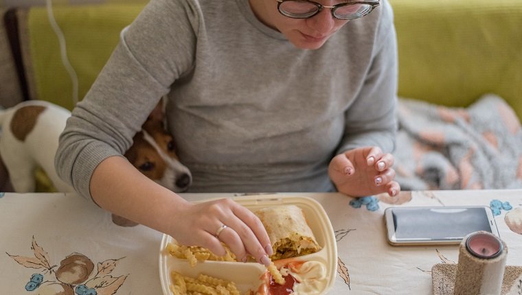 Junge Frau mit Brille isst Fast Food zu Hause