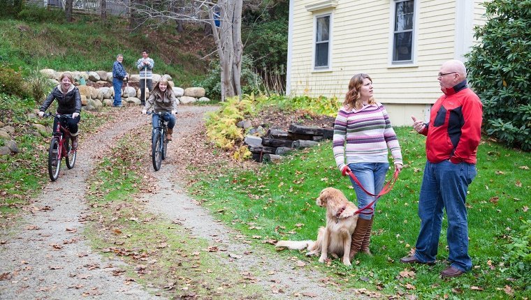 Nachbarschaftsszene Teenager Radfahren Familie Herbst - Nachbarn plaudern, während Hund spazieren gehen und im Garten arbeiten