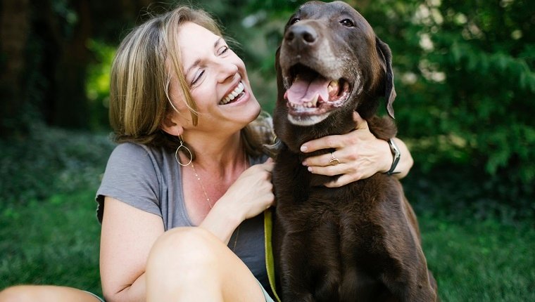 Lächelnde Frau, die auf Gras mit Labrador Retriever sitzt