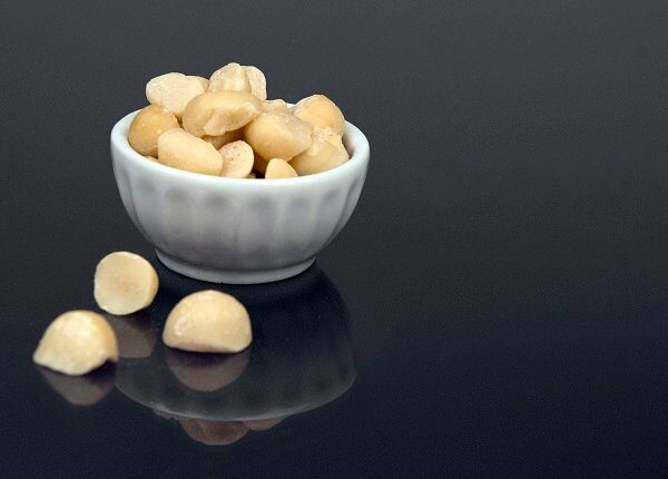 A small snack-size bowl of macadamia nuts (or ingredient size bowl) sits on a black reflective surface.