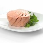Canned tuna portion served on white dish with parsley.