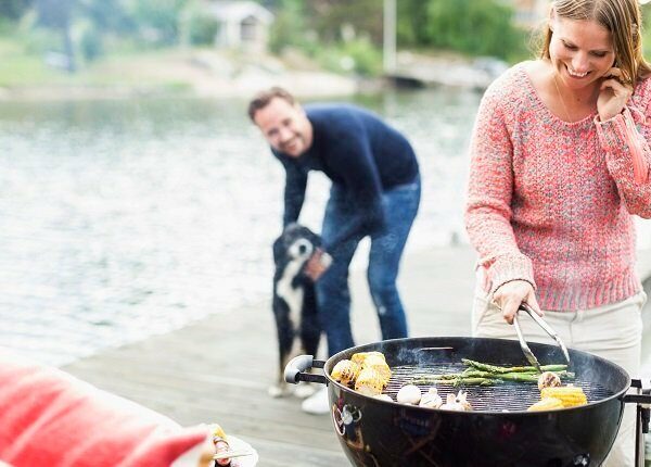 Happy woman using mobile phone while barbecuing with man and dog in background on pier