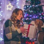 Young smiling couple is celebrating Christmas holidays with their beagle dog, giving it a present for the holidays.