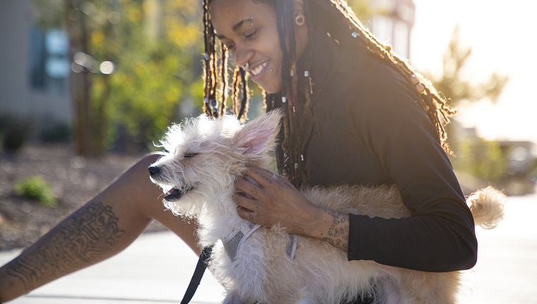 Eine androgyne afroamerikanische Person mit einem Hund draußen in einem Park.