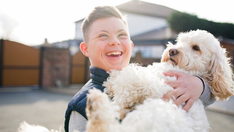 A boy with down syndrome hugs his pet dog in the driveway.