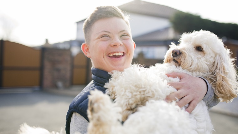 Ein Junge mit Down-Syndrom umarmt seinen Hund in der Einfahrt.