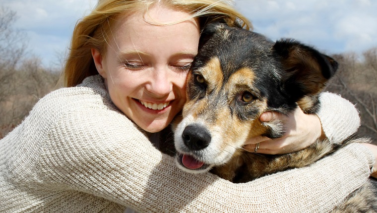 ein liebevolles und offenes Porträt einer glücklichen Frau, die ihren großen Deutschen Schäferhund umarmt.