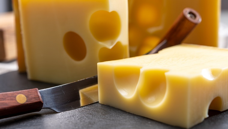 Block Schweizer mittelharter gelber Käse Emmentaler oder Emmentaler mit runden Löchern und Käsemesser aus nächster Nähe