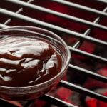 A bowl of BBQ sauce on the grill.