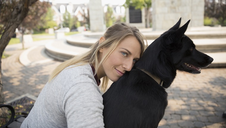 Liebevolle Tierbesitzerin, die schwarzen Hund im Park umarmt