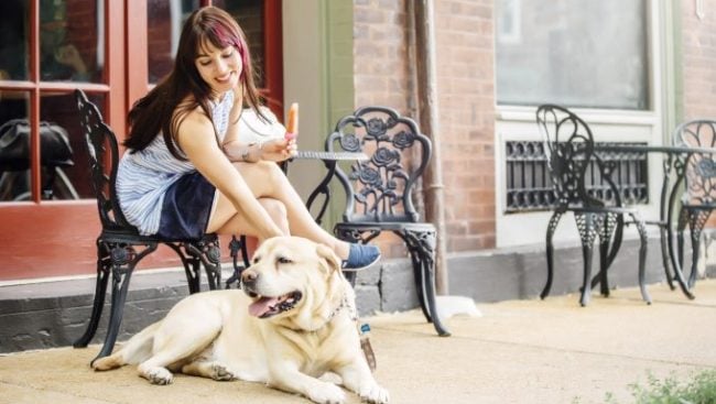 Eine Frau lächelt und streichelt ihren Labrador in einem Straßencafé.