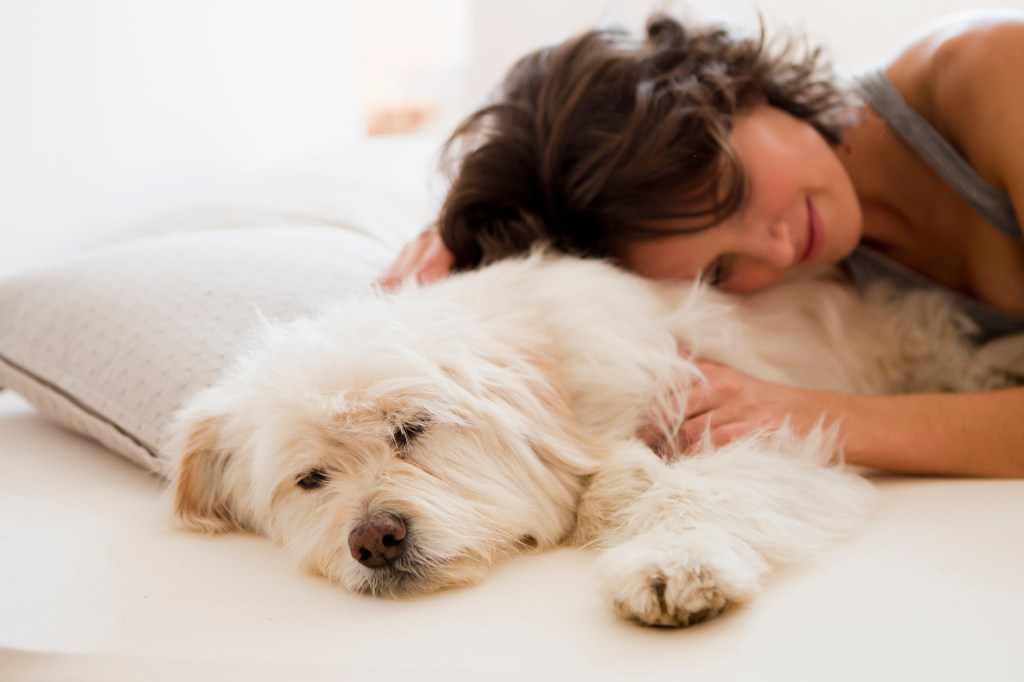 Frau entspannt sich mit ihrem Hund im Bett.